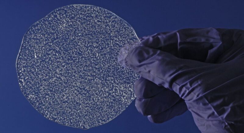 Image of a transparent disk against a blue background. The disk has lots of air bubbles embedded in it.
