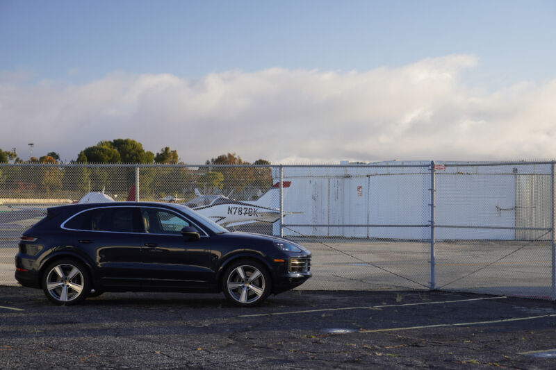 A Porsche Cayenne parked next to a chain link fence by a general aviation airport