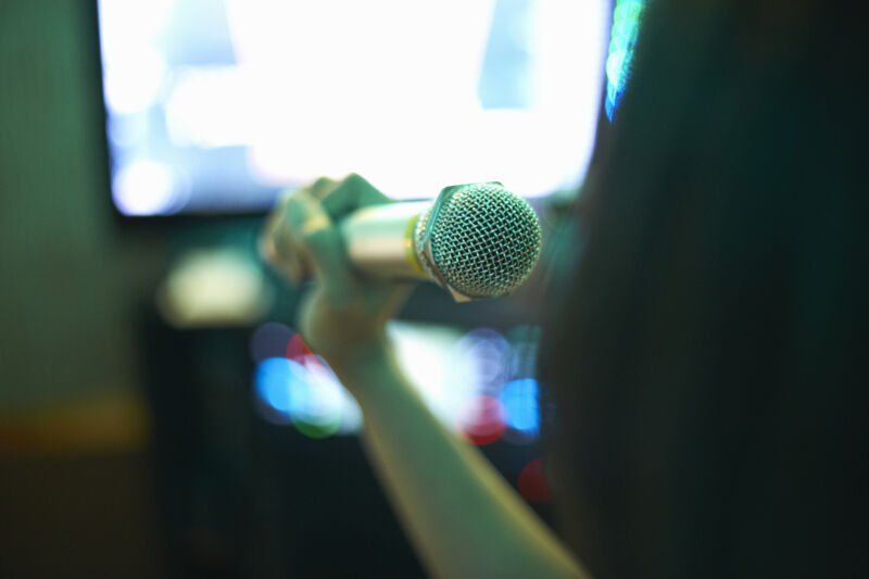 A hand holding a microphone against a blurry backdrop, taken from an angle that implies the microphone is directly in front of your face.