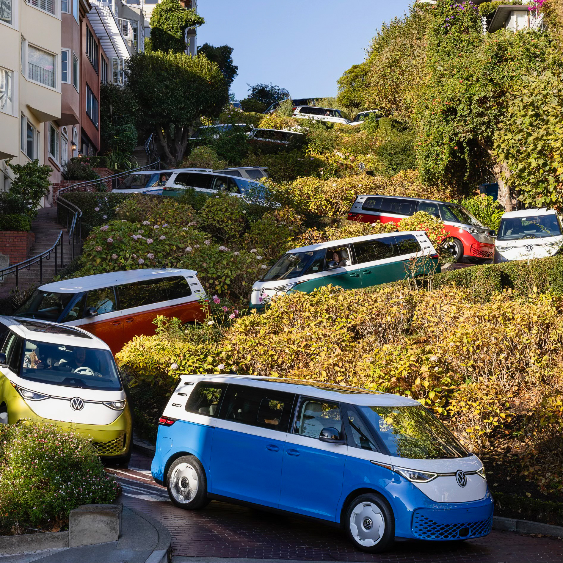 A convoy of brightly colored VW ID Buzzes drives down Lombard St in San Francisco.