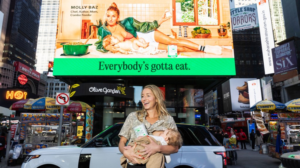 Woman breastfeeding a baby in front of a billboard