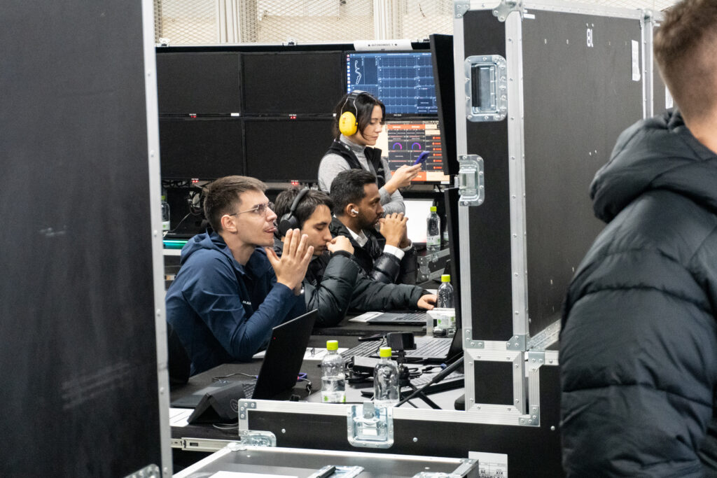 A group of engineers look at monitors in a race track garage.