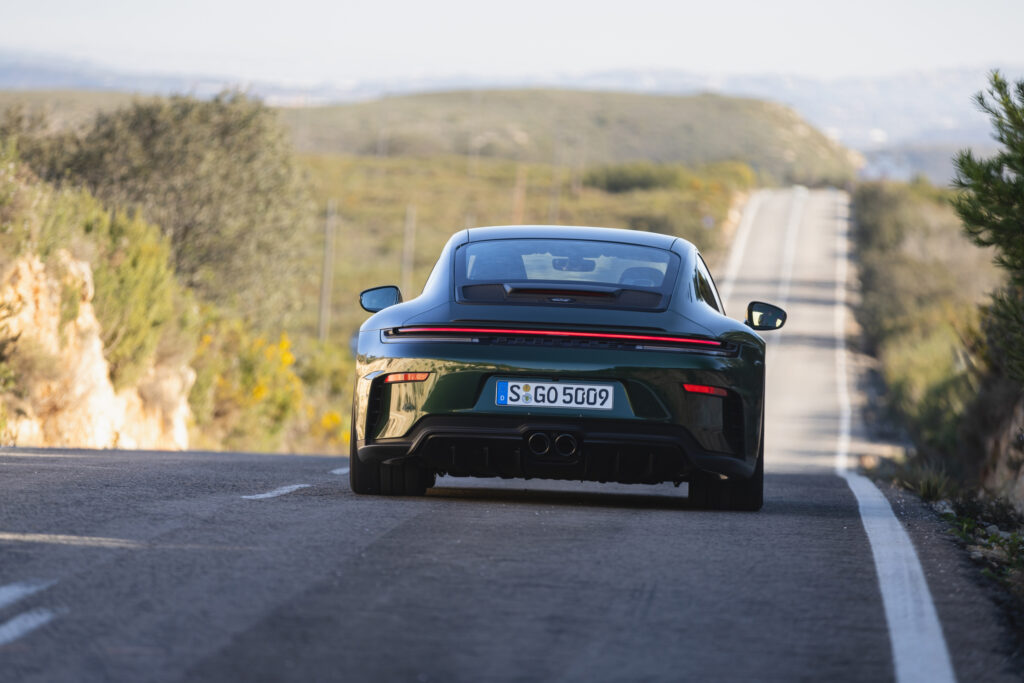 A green Porsche 911 GT3 drives away from the camera