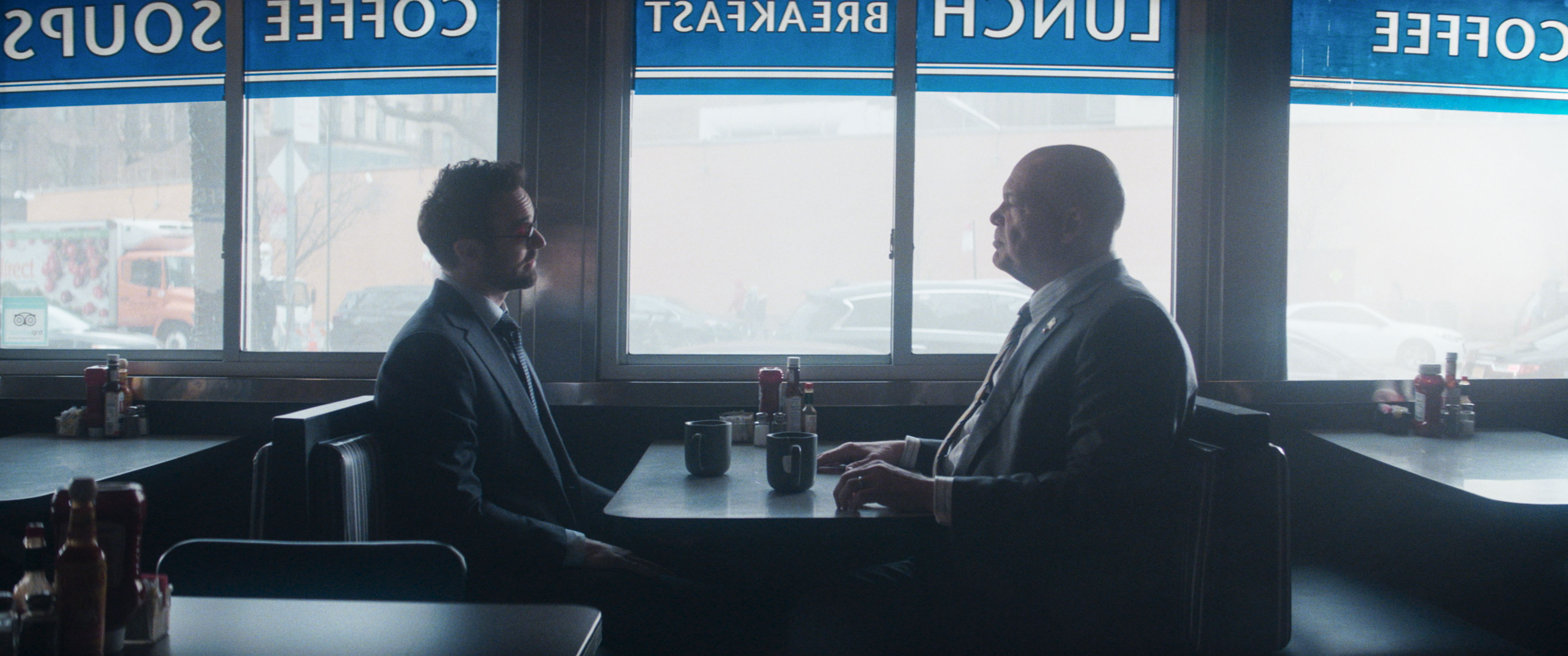 Two men in suits sitting across from one another in a both at a diner.