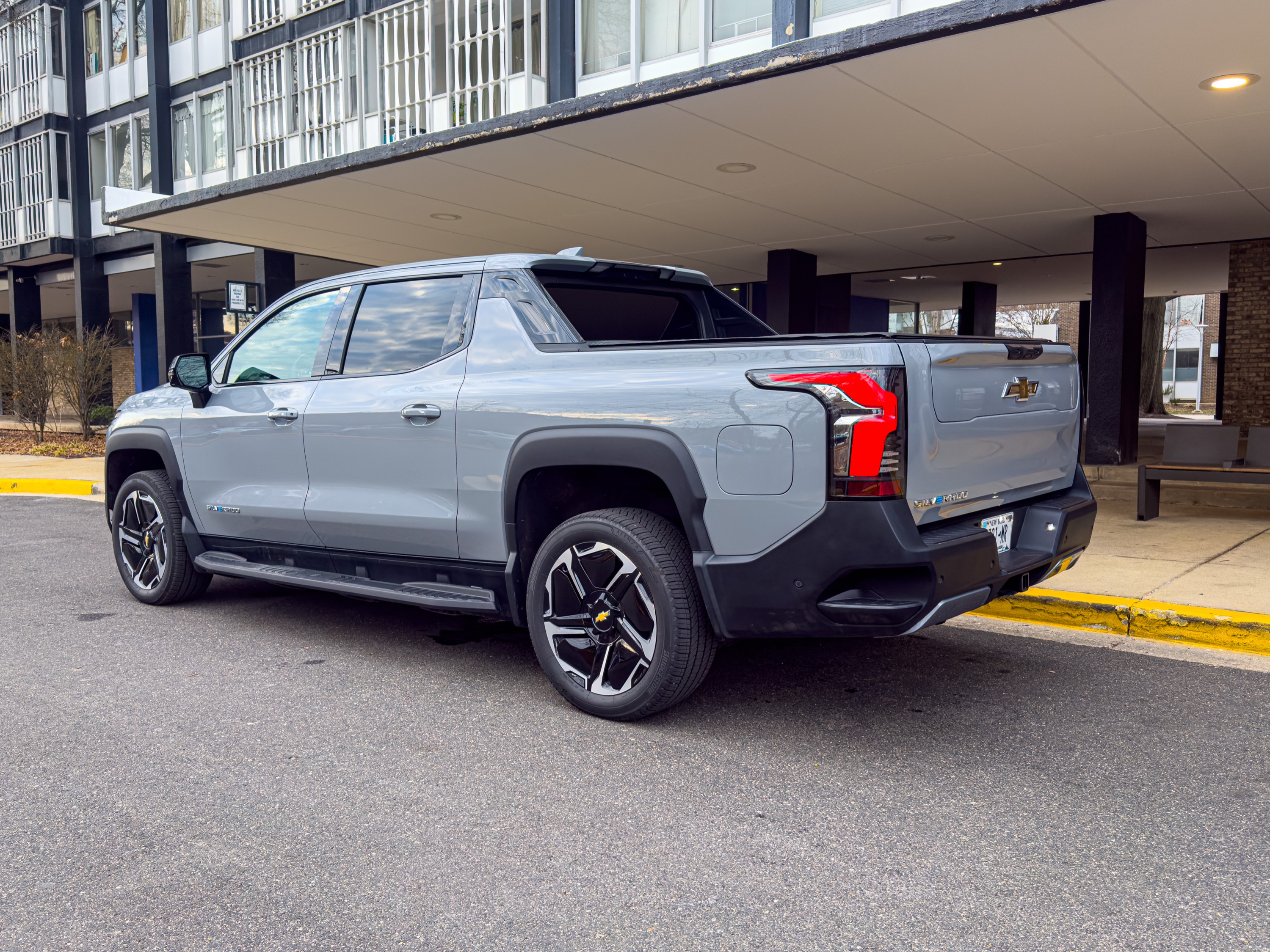 A chevrolet Silverado EV seen from the rear 3/4, parked in front of a mid-century building