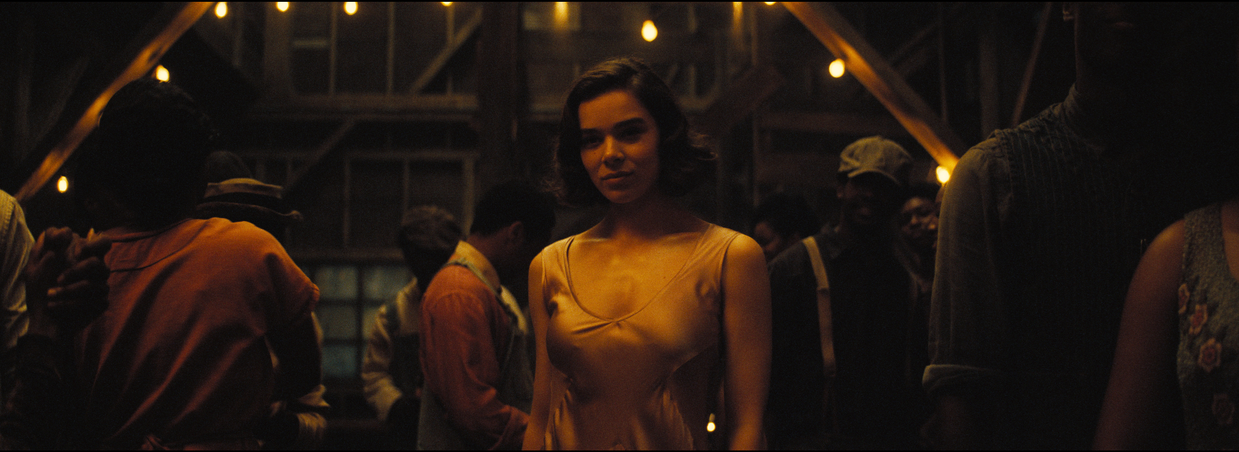 A woman in a satin dress standing in a wooden building that’s been converted into a juke joint. Around the woman are other people dancing.
