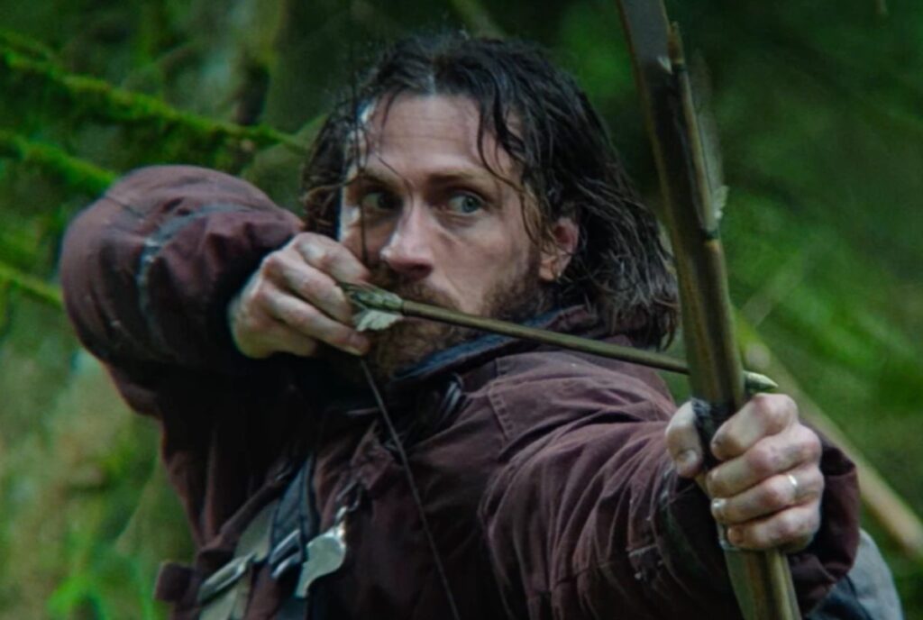 closeup of bearded man with an arrow cocked and ready to fire.