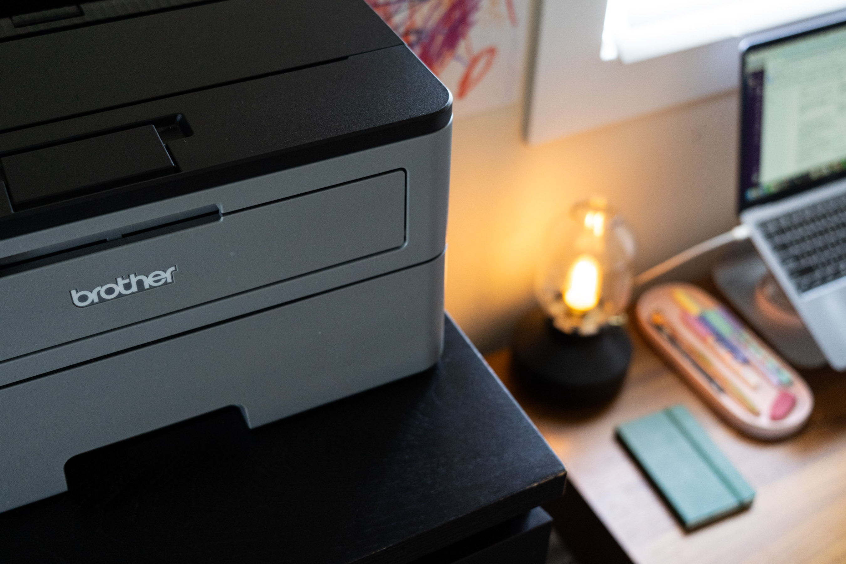 A closeup of a printer and looking down at the desk next to it, showing a lit lamp.