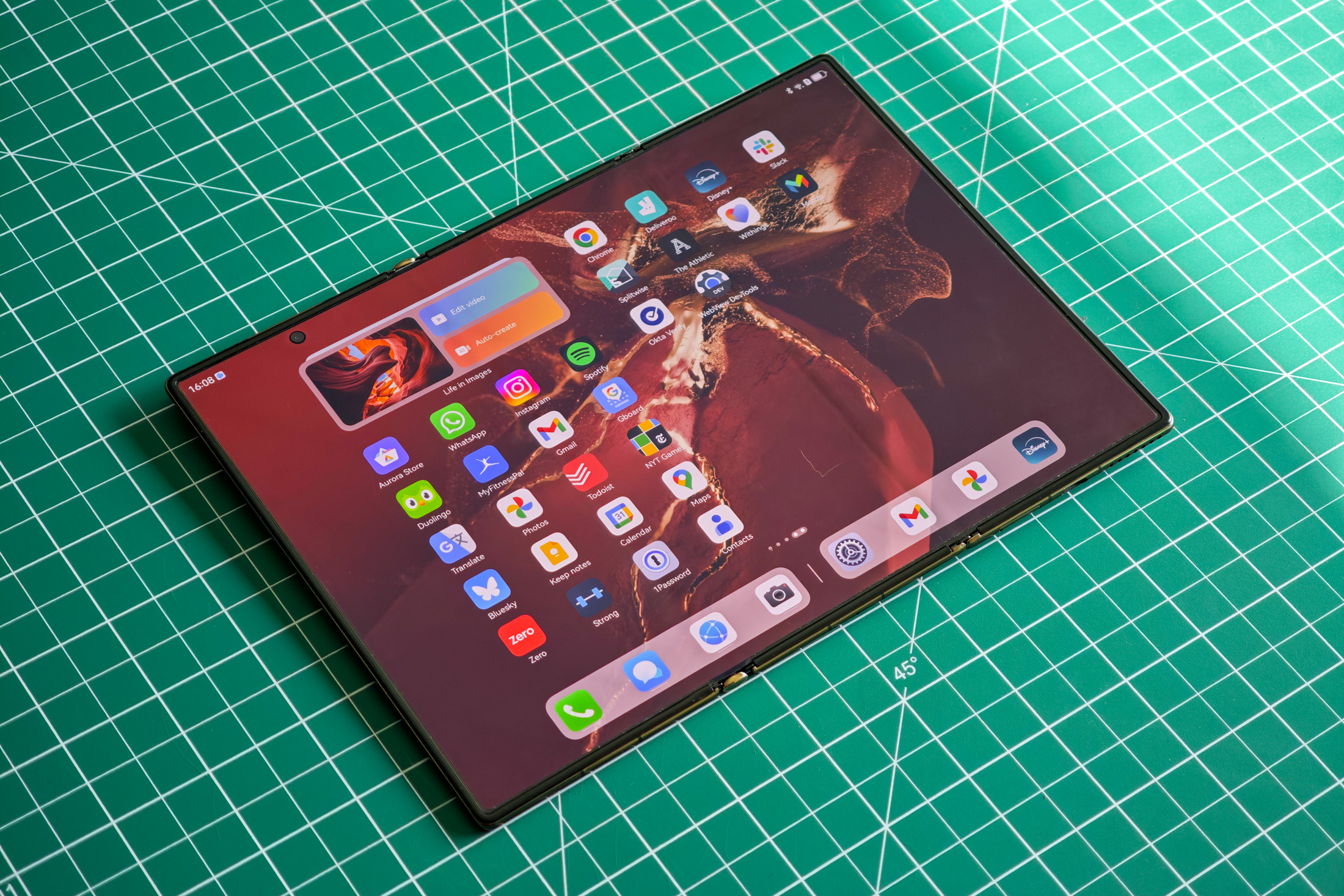 Huawei Mate XT flat on a green table fully unfolded.