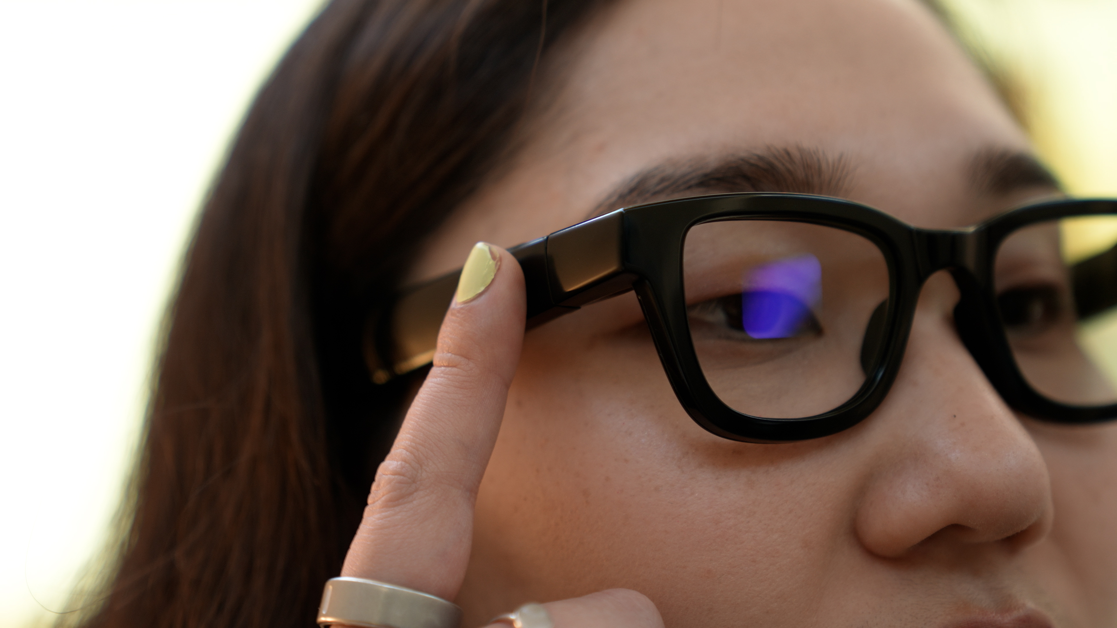 Closeup of senior reviewer Victoria Song tapping the side of the Android XR prototype glasses to bring up Gemini.
