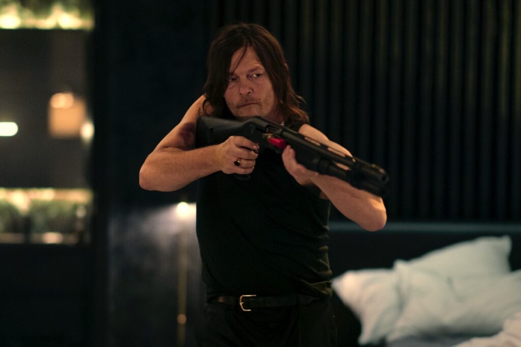 Man in shortsleeved black tee and jeans pointing a high=powered rifle