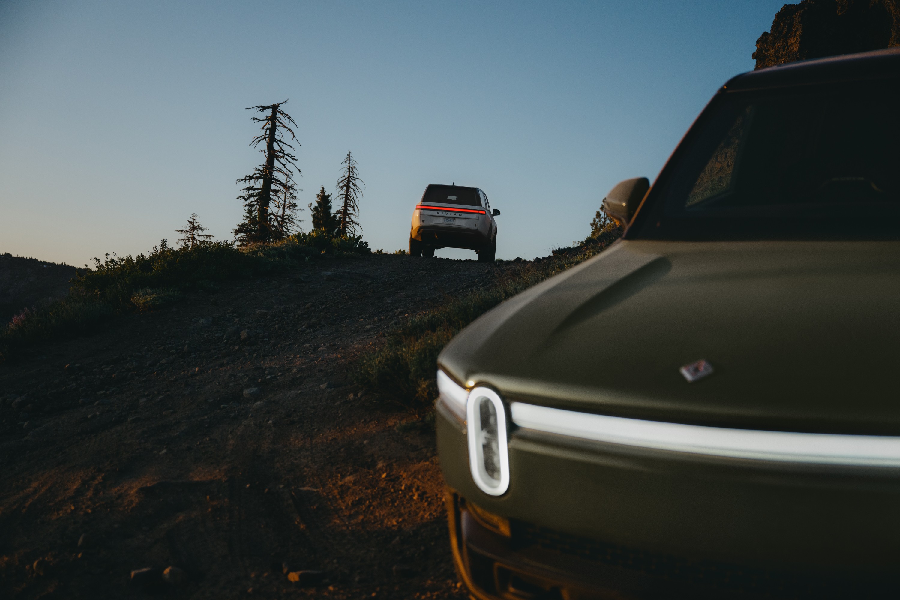 A pair of Rivians seen off-road at dusk.