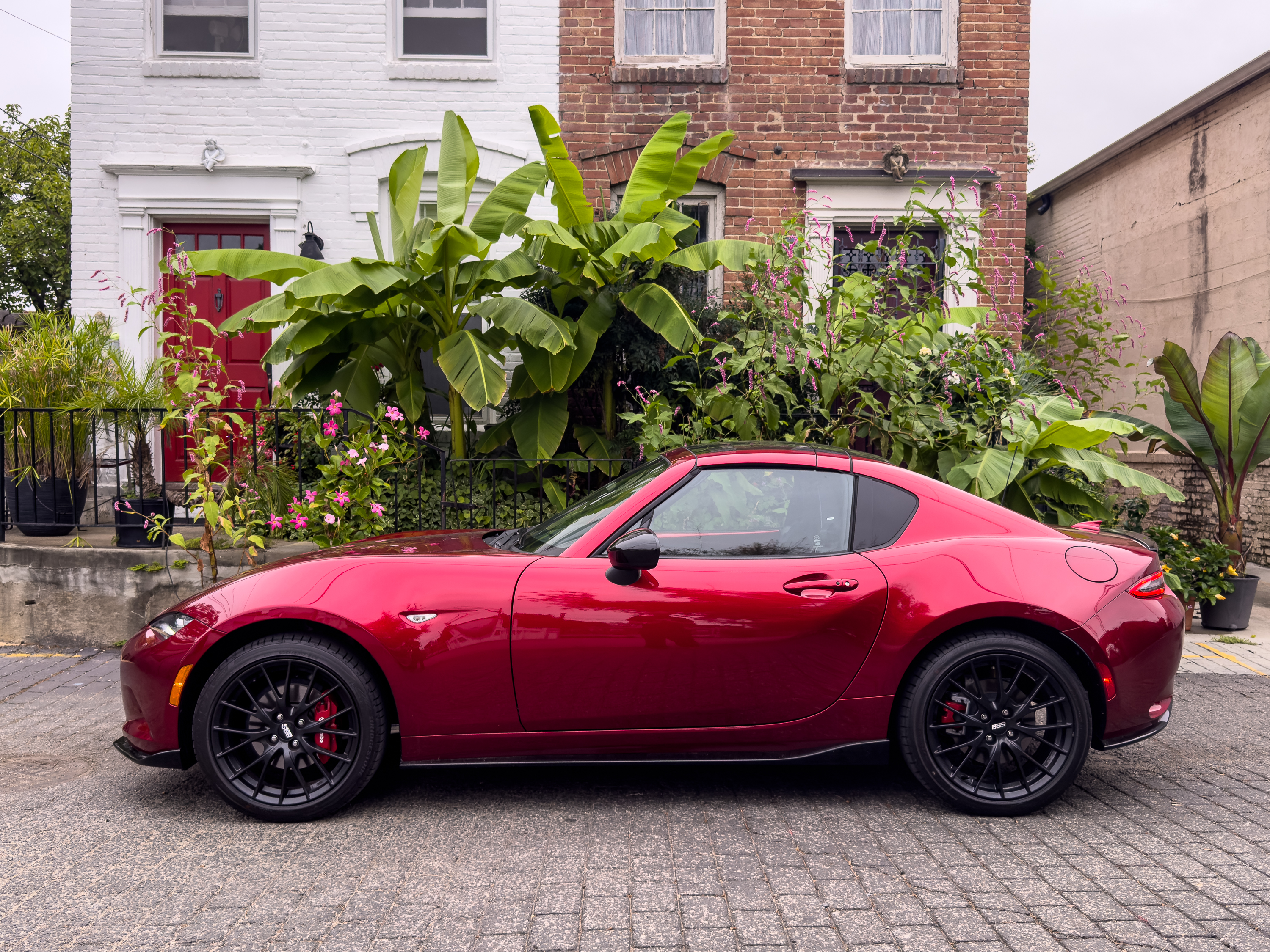 A red Mazda MX-5 Miata RF parked in front of two townhouses