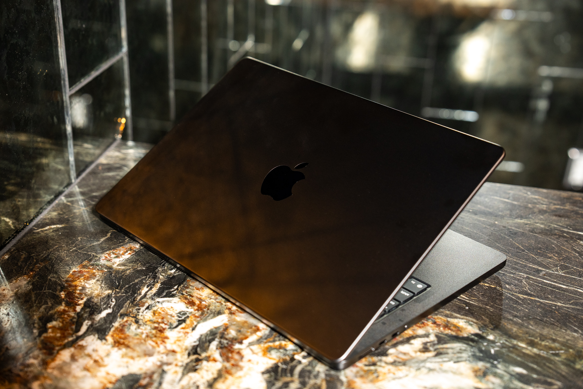 A 2025 14-inch MacBook Pro M5 on a marble bar top, turned away from the camera and partially closed to show its lid and logo.