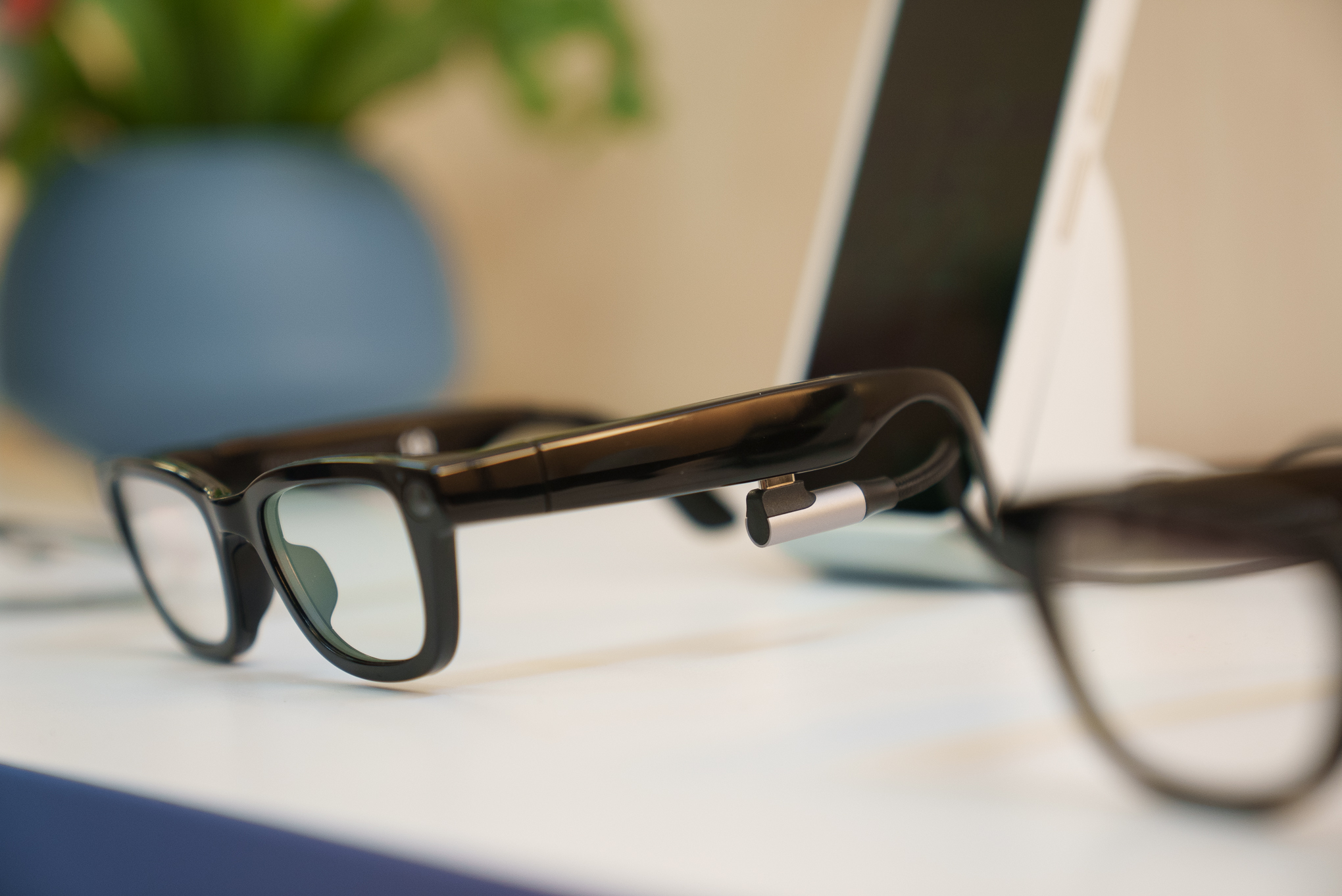 Close up of Google’s Prototype AI glasses from a side angle at Google I/O. In the background you can see a smartphone and vase with plants.