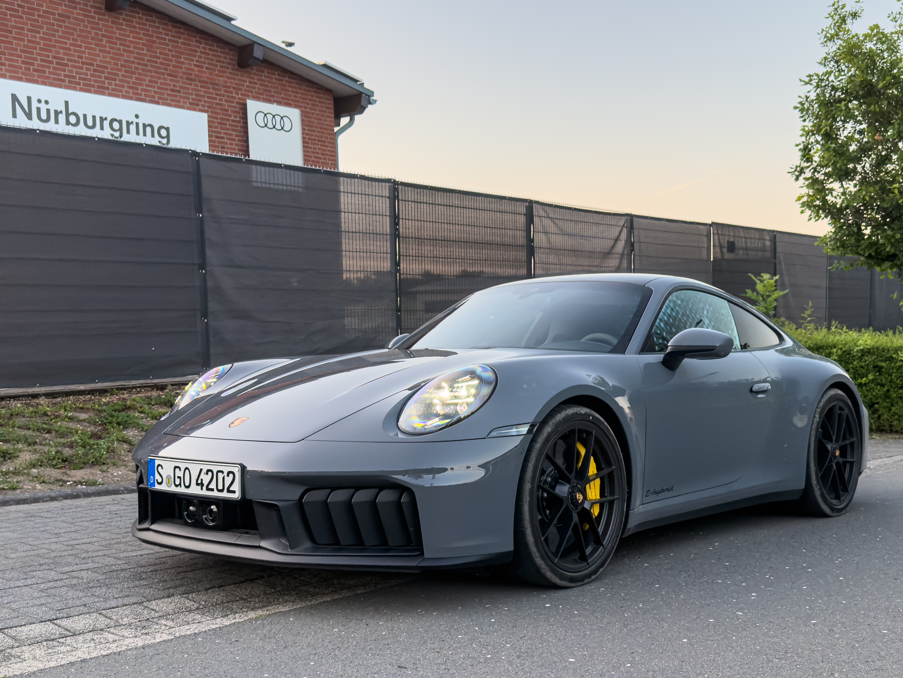 A grey Porsche 911 parked outside a building with an Audi logo and Nurburgring on the side.