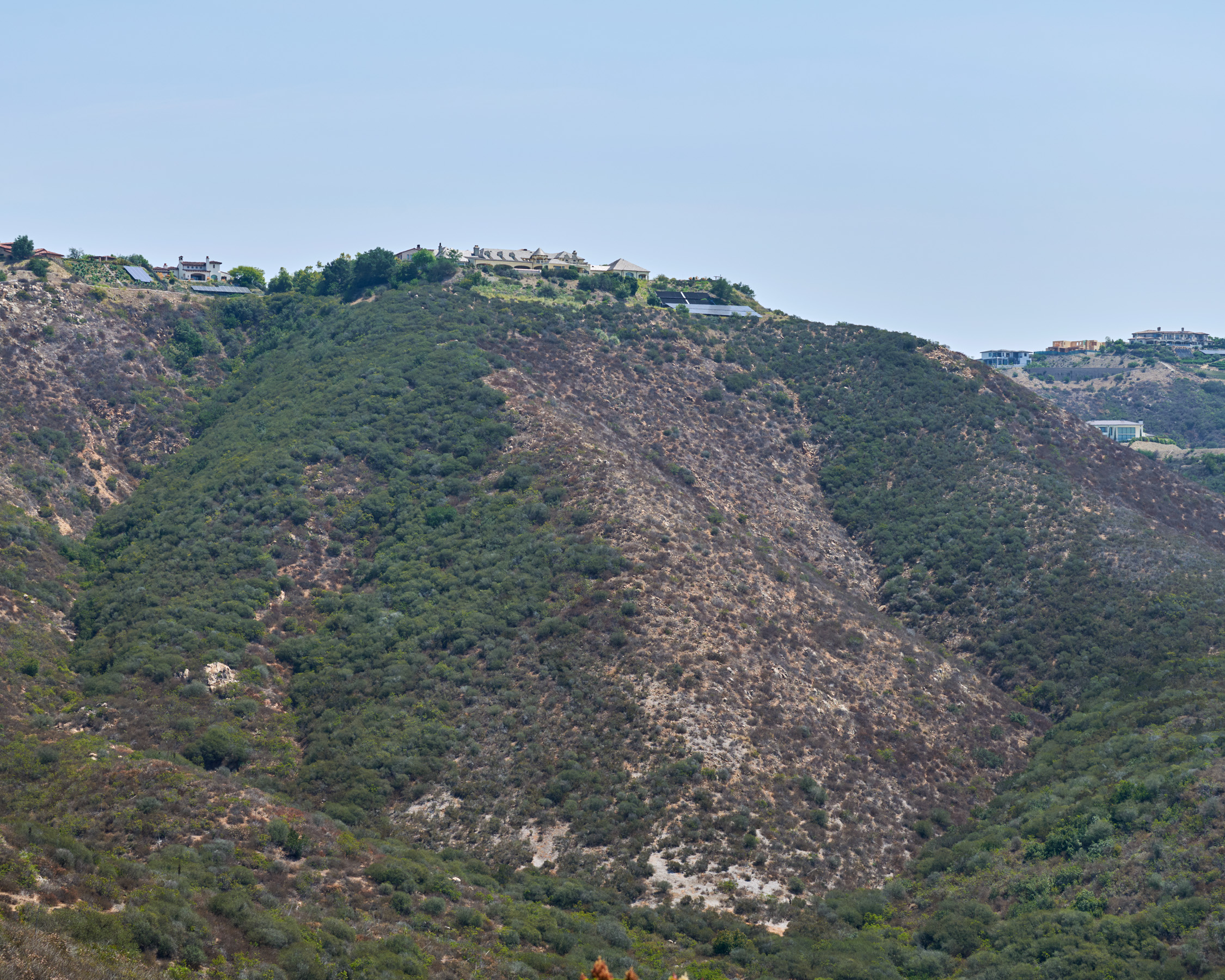 The side of a hill, with brown patches where fires burned vegetation