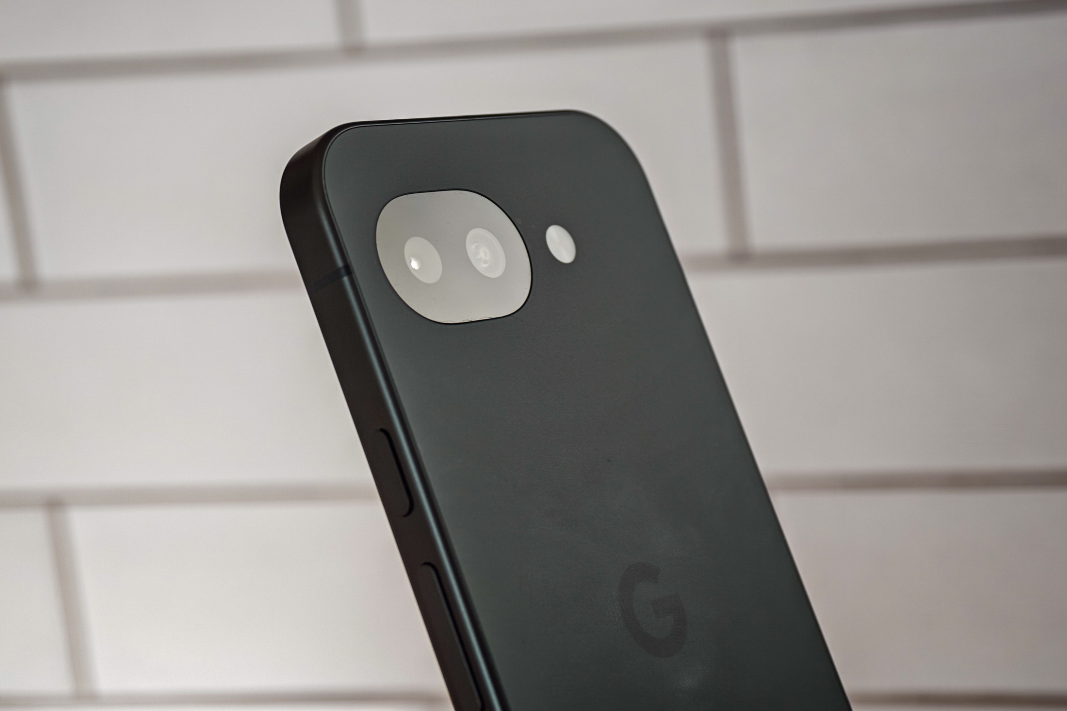 Photo of Google Pixel 10A in front of white tiles, showing the camera from an angle