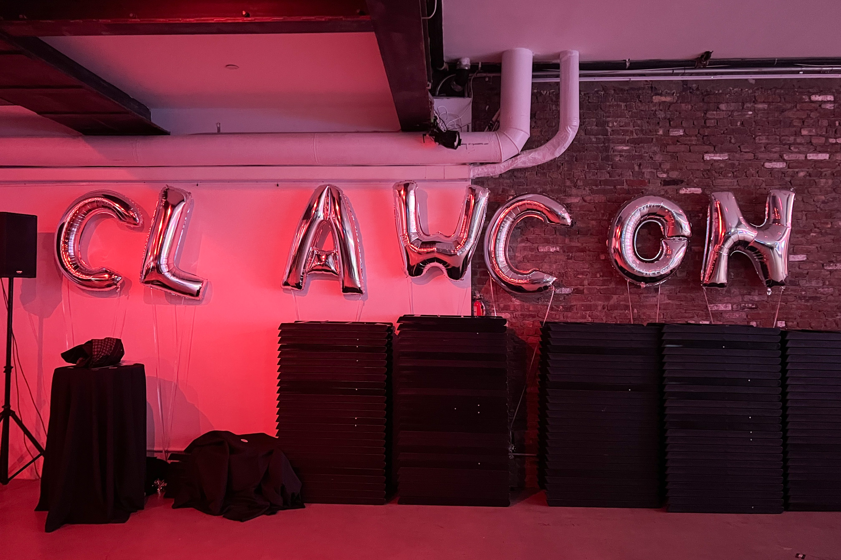 An image of a room with pink lighting and silver balloons spelling out CLAWCON.