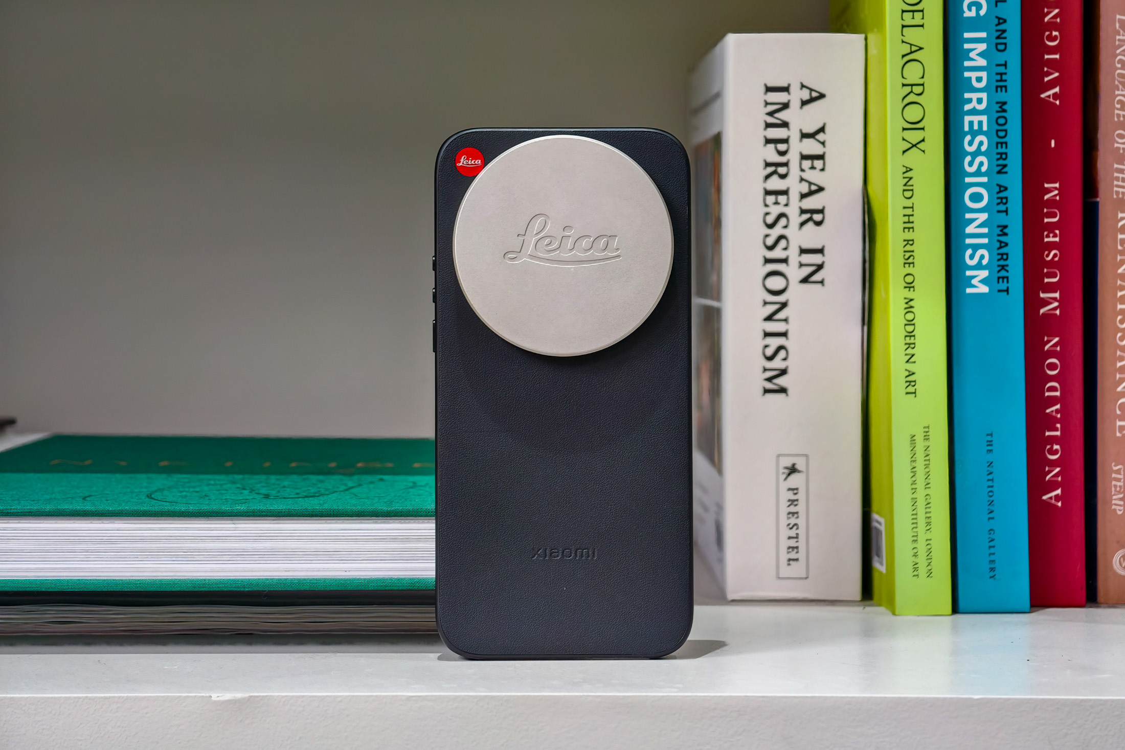 Photo of the Xiaomi Leica Leitzphone on a bookshelf, in a case with a Leica lens cap