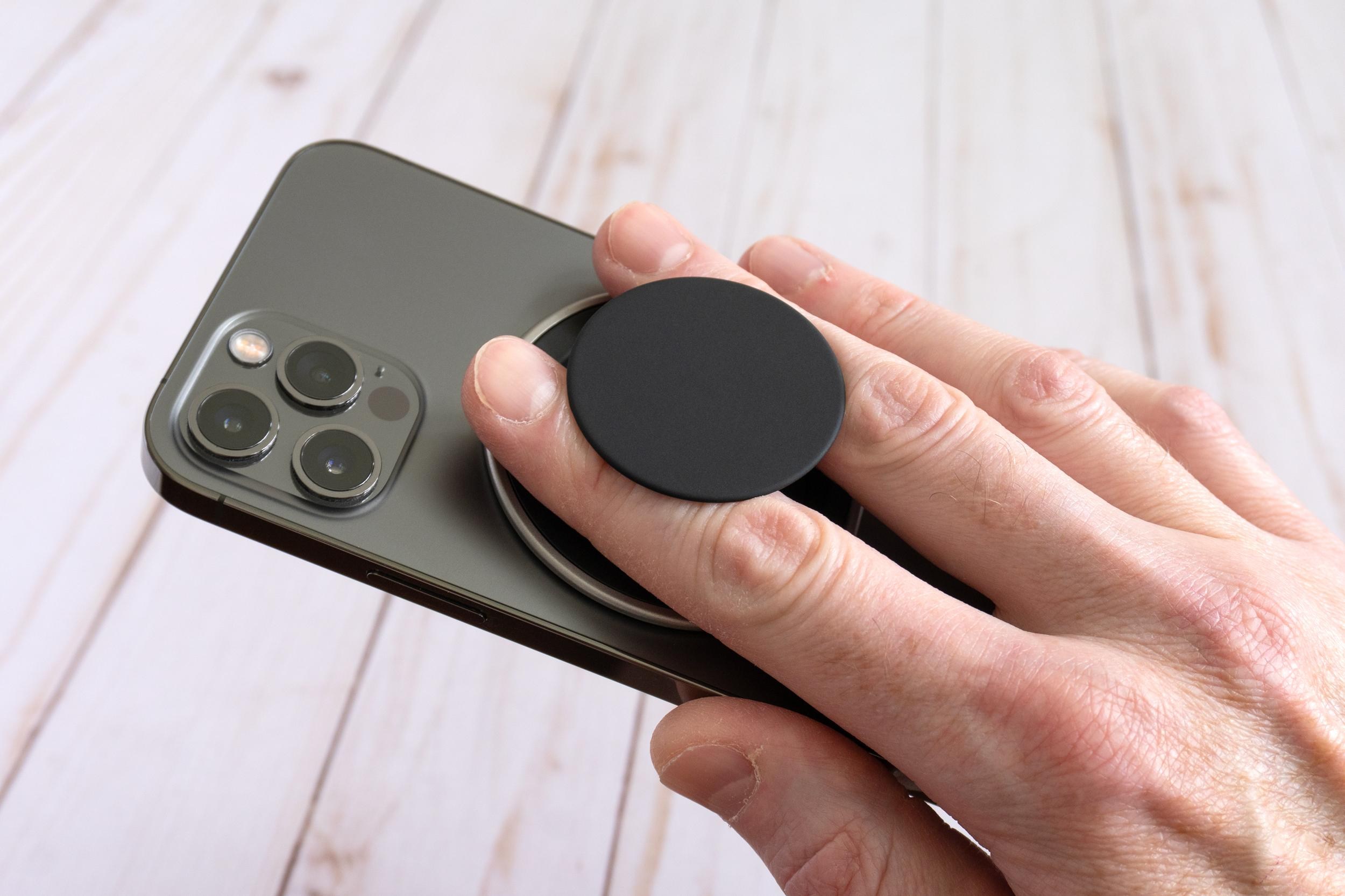 A person holds an iPhone 12 Pro using the PopSockets Low-Pro grip attached to the back.