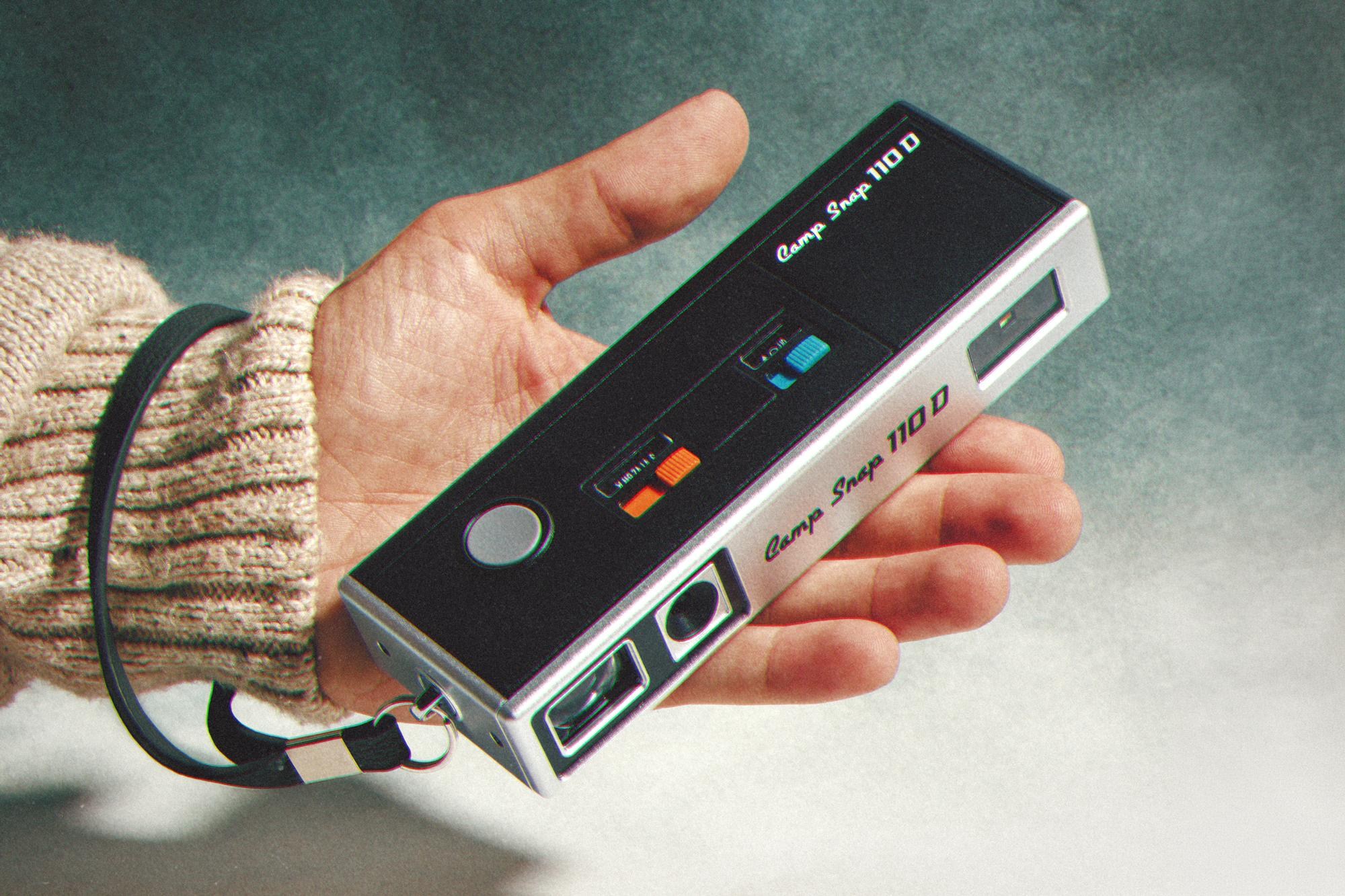 A person holds the Camp Snap 110D camera in their left hand.